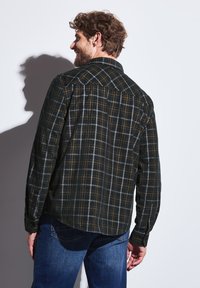 Černá kostkovaná košile se zelenými, bílými a oranžovými pruhy. Obsahuje límeček a manžety na knoflíky. Nositelná s modrými džíny, zobrazující zadní pohled.