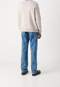Light gray sweatshirt with ribbed cuffs and hem, paired with blue denim jeans featuring back pockets and a straight leg fit. Black shoes.
