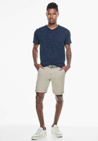 Námořnické tričko s V-výstřihem, světle béžové krátké kalhoty s ohrnutými nohavicemi a bílé tenisky s černými akcenty. Hladká tkanina, moderní střih a minimalistický design.