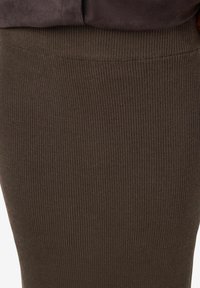 Jupe marron côtelée avec une finition texturée et une large ceinture élastique. Le tissu semble doux et extensible, adapté au confort et à l'ajustement.