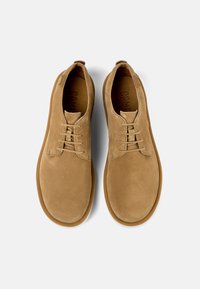 Scarpe in camoscio di colore beige chiaro con punta arrotondata e design con lacci. Presentano una suola in gomma e una texture morbida per il comfort.