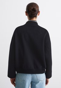 Sort, oversized sweater med høj hals, ribbede manchetter og kant, lavet af blødt stof; parret med lyseblå, afslappede jeans.