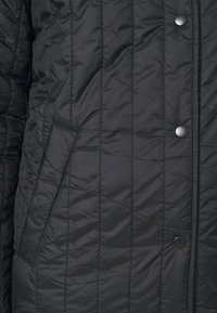 Chaqueta acolchada negra con una textura suave y brillante, costuras horizontales y cierres de botones a presión. Incluye bolsillos laterales para almacenamiento.