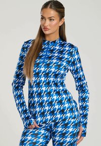 Langsleeve sporttop met een blauw, zwart en wit houndstoothpatroon, rits-halsontwerp en aansluitende pasvorm. Glad, rekbaar materiaal.
