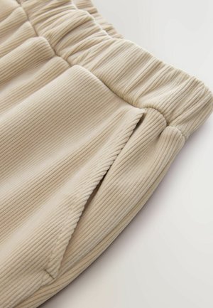 Beige Rippstoff-Jogginghosen mit einem gerafften Bund und Seitentaschen, die eine weiche Textur und ein lässiges Design zeigen.
