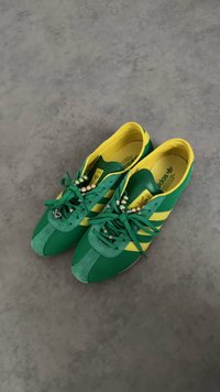 Zeleni in rumeni Adidas copati z biseri nanizanimi na vezalke, počivajo na sivi betonski tleh.