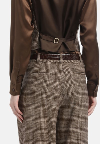 Bruine satijnen blouse met een sluiting aan de achterkant, gecombineerd met bruin check-gepatenteerde broeken en een glanzende bruine riem.
