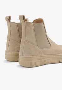 Bottines beiges en suédine avec des panneaux élastiques sur les côtés. Elles possèdent une semelle striée et des languettes pour un enfilage facile.