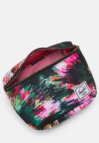 Prostokątny worek na zamek błyskawiczny z żywym, abstrakcyjnym wzorem kwiatowym, częściowo otwarty, ukazujący czerwono-białą, pasywną podszewkę oraz etykietę marki Herschel.