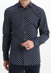 Marineblauw overhemd met knopen en een patroon van witte stippen, lange mouwen en een klassieke kraag met een zachte katoenen textuur.