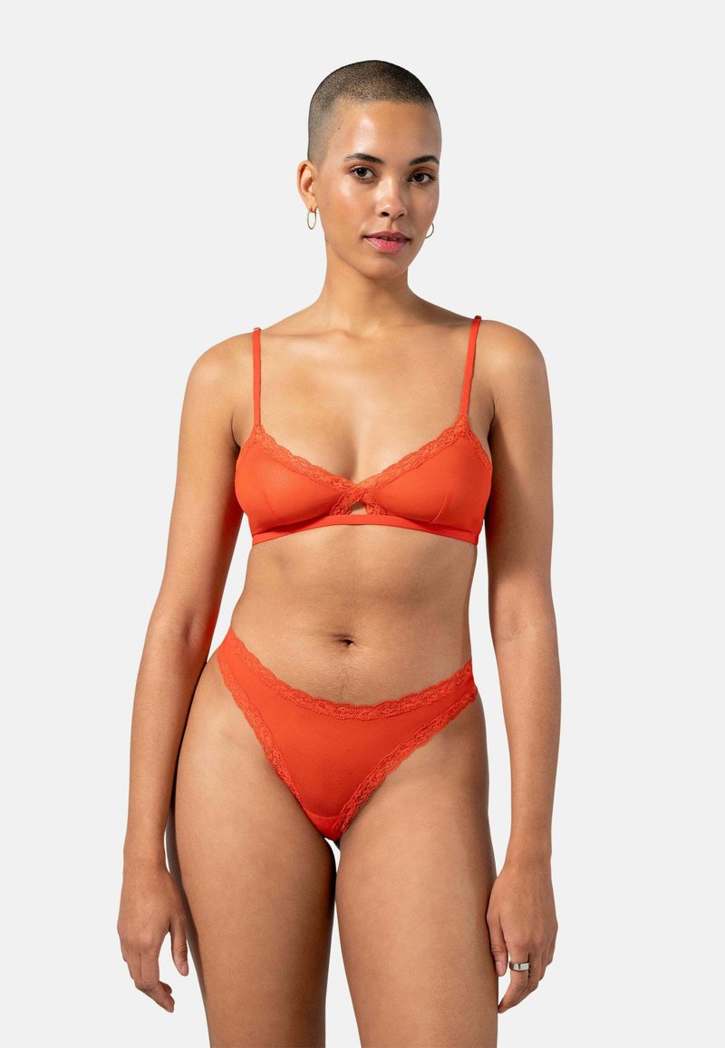 Bralette rouge avec des bordures en dentelle et un string assorti, présentant des bretelles ajustables, un tissu lisse et un délicat accent en dentelle florale sur les bords.