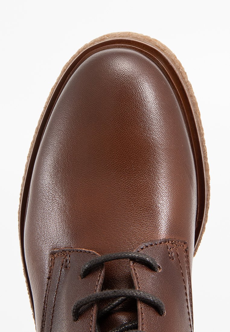 Braunes Leder-Schuh mit glatter Textur, runder Zehenpartie und schwarzen Schnürsenkeln. Die Sohle ist hellbraun mit einem robusten Muster für guten Halt.