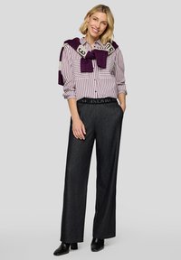 Striped button-up shirt in white and purple, paired with high-waisted dark denim trousers and a purple sweater tied around the shoulders.