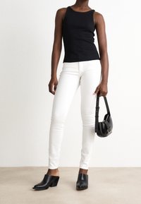 Svart åtsittande linne, vita smala jeans och svarta klackskor. Bär en liten svart handväska med axelrem. Släta texturer.