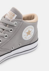 Szary wysokoprofilowy tenisówka na płótnie z białą gumową podeszwą, metalowymi oczkami, beżową wyściółką oraz okrągłą naszywką z logo przedstawiającym gwiazdę.