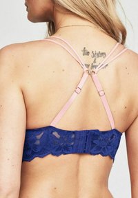 Marinblå spetsbehå med justerbara rosa band, blomtextur och hak-och-ögla-stängning baktill. Har vågiga kanter.