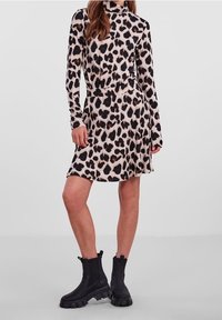 Abito leopardato a maniche lunghe con una silhouette aderente, realizzato in tessuto morbido; abbinato a stivali neri alti alla caviglia con suole spesse.