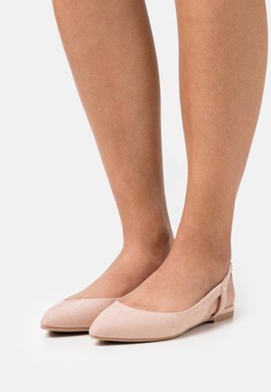 Pieds portant des ballerines à brides arrière en suède rose pâle avec des bouts pointus sur fond blanc.