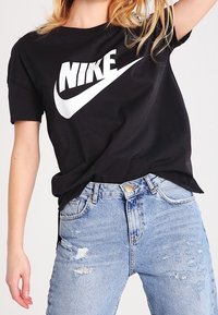 Schwarzes Baumwoll-T-Shirt mit einem weißen Nike-Logo, kombiniert mit hellblauen, ausgewaschenen Jeans, die fransige Kanten und sichtbare Nähte aufweisen.