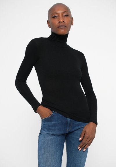 Maglia nera a maniche lunghe con colletto a imbuto, design aderente, texture morbida, abbinata a jeans di denim blu. Nessun motivo o decorazione distintiva.