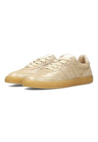 Zapatillas de cuero dorado con un acabado texturizado, cordones planos en beige y suela de goma. Presenta tres rayas a cada lado.