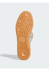 Potplat tenisice u svijetlosmeđoj gumi s teksturiranim uzorcima, kružnim detaljima i utisnutim logotipom u sredini.