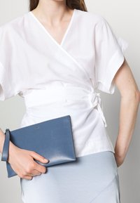 Bílý top s volnými rukávy, doplněný světle modrou sukní a modrou koženou kabelkou s poutkem na zápěstí. Výrazné texturované materiály.