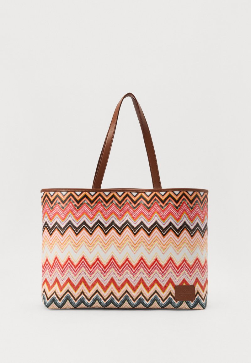 Värikäs kassi, jossa on zigzag-kuvio pinkissä, oranssissa ja mustassa. Varustettu ruskeilla nahkahandleilla ja pienellä nahkatalogotunnuksella.