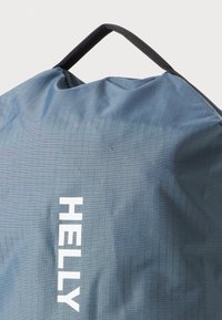 Modrá textilná taška s textúrovaným mriežkovým vzorom. Obsahuje čiernu rúčku a biele logo "HELLY". Hladký povrch s jemným leskom.
