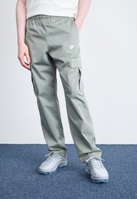 Νάιike cargo παντελόνι σε ανοιχτό πράσινο ύφασμα, με ελαστική μέση και πλαινές τσέπες. Συνδυασμένο με γκρι αθλητικά παπούτσια.