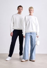 Weiße Sweatshirts, marineblaue Trainingshosen, hellblaue, weit geschnittene Jeans und weiße Schuhe. Minimalistische Accessoires, einschließlich einer kleinen weißen Tasche.