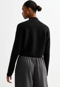 Pull noir côtelé avec un col montant, doté de manches longues et d'un design court, associé à un pantalon gris à taille élastique.