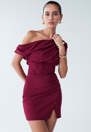Off-the-shoulder, short dress in deep burgundy fabric with a fitted bodice, draped neckline, and side slit. Smooth texture, form-fitting design.