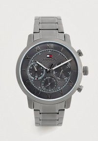 Orologio da polso Tommy Hilfiger con cinturino in metallo grigio, quadrante nero, numeri Romani, tre sottodials che mostrano funzionalità di 24 ore, giorno e data.