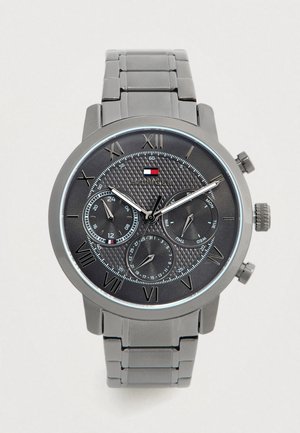 Reloj de pulsera Tommy Hilfiger con correa de metal gris, esfera negra, números romanos, tres subesferas que muestran la hora en formato de 24 horas, día y funciones de fecha.