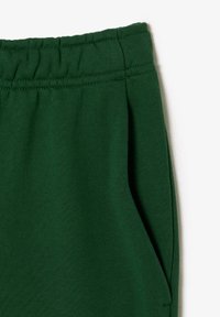 Gröna byxor med elastiskt midjeband som visar sidofack och sömdetaljer mot en enkel vit bakgrund.