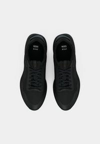 Μαύρα αθλητικά παπούτσια με άνω μέρος από λείο ύφασμα, στρογγυλή μύτη και αντίθετους κορδόνια. Διαθέτουν υφασμάτινη σόλα και λογότυπο στο εσωτερικό.