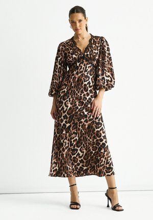 Leopard-print maxi dress made of silky fabric, featuring a V-neckline, puff sleeves, and a flowing design. Black strap heels accent the look.