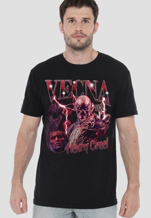 Mann trägt ein schwarzes T-Shirt mit rotem Grafikdruck monströser Figuren und dem Text "VECNA 001 Henry Creel" auf der Vorderseite.