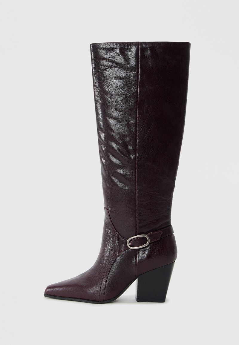 Burgundy leather knee-high boots with a pointed toe, textured finish, and a block heel. Features a strap with a silver buckle accent.
