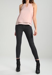 Top senza maniche di un delicato rosa chiaro, con scollo a chiave, design a strati, abbinato a jeans neri attillati e stivaletti neri alla caviglia.