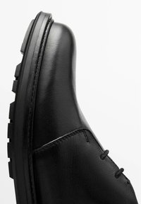 Botte en cuir noir à bout arrondi, avec des coutures apparentes et une surface texturée. Semelle épaisse noire avec un dessin de crampons proéminent.