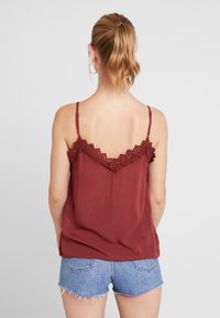 Top sin mangas burdeos con encaje en el escote, hecho de una tela ligera, combinado con pantalones cortos de mezclilla claros, visto desde la espalda.