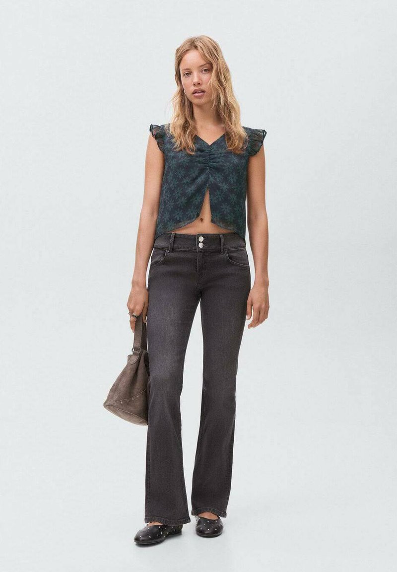 Top corto con stampa floreale scura e maniche corte a balze, abbinato a jeans neri a campana e calzature nere con borchie. Accessorio: borsa marrone.