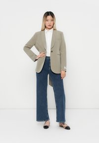 Svetle šedý blazer s jemným proužkem a jedním knoflíkem, kombinovaný s bílou košilí s límečkem a modrými širokými džínami, doplněný černými balerínami.