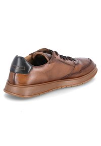 Brown leather sneaker with a smooth finish, black heel accent, round toe, and black laces. Features a textured rubber sole.