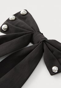 Black fabric bow with multiple pleats, featuring silver dome-like embellishments and a central knot, focusing on texture and design details.