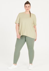 Lys grøn kortærmet skjorte med en afslappet pasform, parret med olivengrønne leggings. Hvide sneakers fremhæver outfittet.