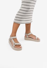 Sandalias de plataforma beige con correas estampadas, hebillas ajustables y parte superior texturizada. Diseñadas para mayor comodidad con una suela más ancha.