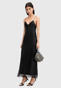 Abito maxi nero in paillettes con scollatura a V profonda e spalline sottili. Presenta una silhouette fluida e una gonna a strati. Abbinato a una borsa testurizzata.